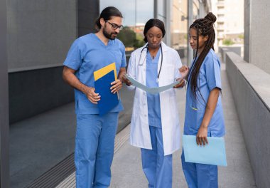 Üniformalı çok ırklı tıp ekibi hastanenin dışında hastanın raporunu okuyor.