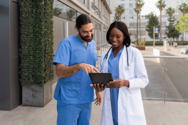 Çok yönlü gülümseyen doktorlar hasta bilgilerini hastanenin dışında tablet kullanarak tartışıyorlar.