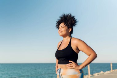 Sahil rıhtımında idmandan sonra ayakta ve nefes alan gözleri kapalı İspanyol bir kadın.