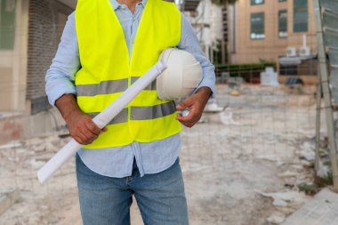 İnşaat alanındaki erkek mühendisin elinde taslak ve başlık var.