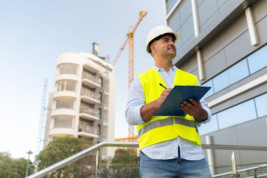 İnşaat mühendisi. İnşaat alanında inşaat işçisi. İnşaat alanındaki bir binayı incelerken panoya not alıyor.
