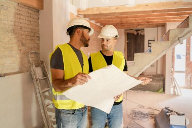 İki erkek inşaat işçisi bina tadilatı sırasında planları tartışıyorlar.