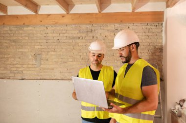 İnşaat alanında dizüstü bilgisayarda iki mühendis ve mimar inşaat planlarını inceliyor.