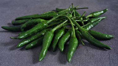 Cayenne. Koyu gri arka planda taze yeşil Cayenne. Capsicum frutescens. Sıcak ve baharatlı. Acı biber ya da kuş gözü kırmızı biber. Endonezya 'da Cabai Rawit olarak da bilinir. Acı biber. Çiğ