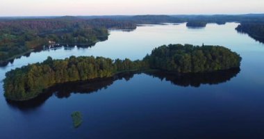 Göldeki küçük yeşil yuvarlak şekilli adalar. Günbatımı renginde bir yaz akşamı. Estonya Fin doğasının hava manzarası. Mavi göl, adalar ve yeşil orman güneşli bir yaz akşamında. 