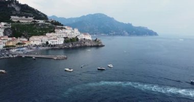 Amalfi Sahili 'nde turistik bir yer Amalfi kayalık yol ve limanı manzaralı. Arka planda büyük mavi dağlar. Ünlü turist yeniden filizlendi. Denizde yüzen tekneler. Yatlar. gemiler. .