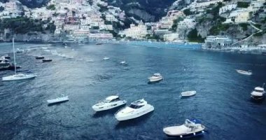 Napoli, İtalya 'da Positano hava manzarası üzerinde uçuyor. Amalfi kıyısındaki beyaz kasaba, beyaz sahil manzarası ve hareket eden ve yüzen tekneleri olan mavi okyanus. Yelkenli, yatlar, demirli gemiler.