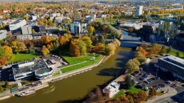 Renkli sonbahar şehrinin üzerinde uç. Yeşil Ciy 'deki binalar. E-ülke Estonya, Tallinn, Tartu 'da sonbahar renkleri. Şehirde nehir kıvrılıyor, şehrin içinde sarı ve turuncu ağaçlar var. Sonbahar günbatımı parlıyor