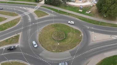 Kavşaktaki araba trafiğinin en üst görüntüsü. Bir sürü arabası ve dairesel kavşağı olan bir trafik çemberi. Yeşil kavşak ve hareket halindeki otobüsleri takip ediyor. Çevre yolunda arabalar ve kamyonlar. 
