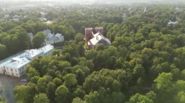 Yeşil ağaçlı şehir parkı, ağaçların ötesindeki şehir silüeti. Yazın gün batımında çekilen insansız hava aracı çok güzel bir siluet sergiliyor. Yürüyen insanlarla, patikalarla, ağaçlarla ve yeşil çimlerle park Eski ortaçağ mimarisi