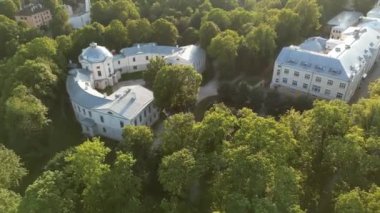 Yeşil ağaçlı şehir parkı, ağaçların ötesindeki şehir silüeti. Yazın gün batımında çekilen insansız hava aracı çok güzel bir siluet sergiliyor. Yürüyen insanlarla, patikalarla, ağaçlarla ve yeşil çimlerle park Eski ortaçağ mimarisi