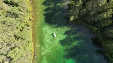 Turkuaz yeşil göl üzerinde şeffaf maden suyu olan bir hava. Şeffaf su manzaralı yeşil çam ağaçlarıyla çevrili, suyun üstünde hareketlilik var. Kürek tahtası gölde hareket ediyor. 