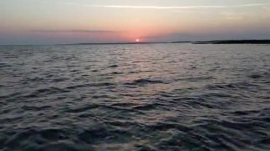 Güneş ufukta batarken okyanus, deniz ya da su üzerinde alçaktan uçuyor. Denizde küçük dalgalar. Denizin üzerinde güneşli bir gün batımı. İHA 'nın su üzerindeki uçuş görüntüsü günbatımını gözler önüne seriyor.. 