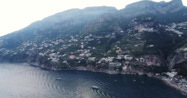 Napoli, İtalya 'daki güzel Positano hava manzarasının üzerinde uçuyor. Amalfi kıyısındaki beyaz kasaba, beyaz sahil manzarası ve hareket eden ve yüzen tekneleri olan mavi okyanus. Şehrin üzerinde uçuyor. 