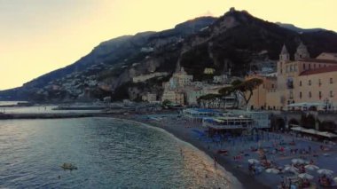 Aerial view of the famous tourist resort of the Amalfi coast. Old town with big large mountains on the background. People sitting nearby the beach. People swimming, blue transparent water. . 