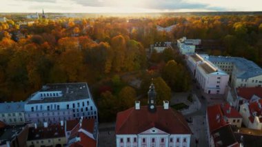 Aerial view of autumn trees in city and roofs of buildings. Colorful autumn trees during sunset, View of Tartu University, Estonia. Forest leaves changing color in Autumn. Tartu town hall,
