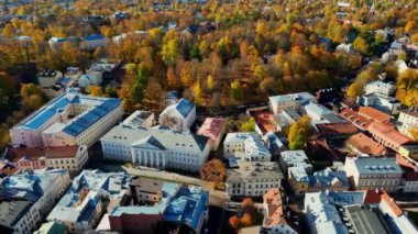 Aerial view of autumn trees in city and roofs of buildings. Colorful autumn trees during sunset, View of Tartu University, Estonia. Forest leaves changing color in Autumn. Tartu University hall. 