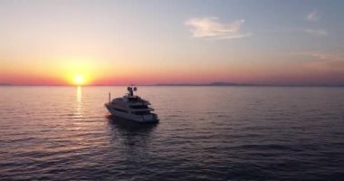 Colorful sunset above the sea surface with sail boat, sun goes down, blue and orange clouds flow in sky. Small yacht boat sailing in calm open sea at sunset. Floating on Sea Surface Golden Sky. 