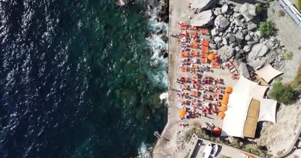 从空中俯瞰着五颜六色的橙色遮阳伞和夏天的人们放松的景象 船离开海湾 透明的蓝色水 有阳光反射的蓝色水面 — 图库视频影像
