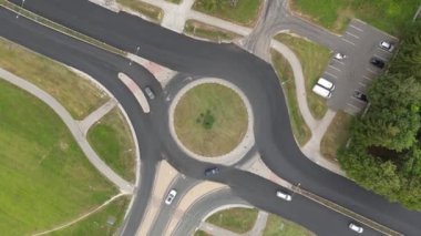 Kavşaktaki araba trafiğinin en üst görüntüsü. Bir sürü arabası ve dairesel kavşağı olan bir trafik çemberi. Yeşil kavşak ve hareket halindeki otobüsleri takip ediyor. Çevre yolunda arabalar ve kamyonlar. 