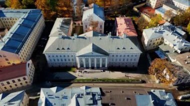 Aerial view of autumn trees in city and roofs of buildings. Colorful autumn trees during sunset, View of Tartu University, Estonia. Forest leaves changing color in Autumn. Tartu University hall. 