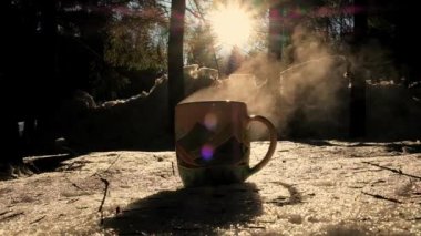 Pouring Tea Into Cup. Hot drink on the background of wild nature. Steaming hot water tea. Traveler Enjoying Hot Tea In Mountain Mug. Hot steamy tea pouring. Cold winter day in forest. 