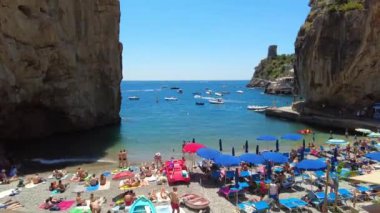 Aerial hyperlapse of clouds and boats at Italy Positano bay full of Boats and ships. Timelapse over the ocean on idyllic island beach tilt up. Crowded beach with tourists enjoying the sun and the sea.