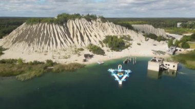 Crystal clear light blue lagoon of Rummu quarry and the adjacent ash hill. Drone shot of white sand mountain by the construction site. Beautiful white sand beach bathed by a turquoise water. 