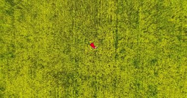 Romantic, dreamy and inspiring wanderlust drone aerial view of young woman in flowing beautiful red dress. Top down shooting with drone in motion from air. Luxury flying silk satin red dress blonde.