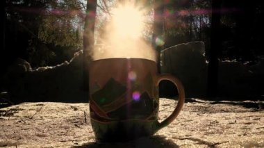 Pouring Tea Into Cup. Hot drink on the background of wild nature. Steaming hot water tea. Traveler Enjoying Hot Tea In Mountain Mug. Hot steamy tea pouring. Cold winter day in forest.