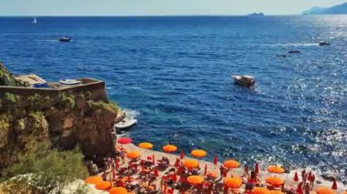 Seawater wave on sandy beach. Positano, Amalfi Coast Famous beach showing colorful sun umbrellas and people relaxing on a summer day. Beautiful white tropical sand beach on a rocky coast summer day. 