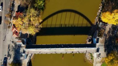 Stunning Aerial shots of bridge over river at sunset with reflection. People walking over bridge that can be seen from reflection. Colorful autumn morning. Trees different colors. Yellow river. 4k 