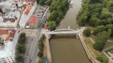 Şehir manzarası. Eski kasaba manzarası. İnsansız hava aracı insanların yaz günbatımında köprüden geçişlerini gösteriyor. İnsansız hava aracıyla uzaklaşıyorum. Yeşil şehir. Estonya, Tartu. Kırmızı çatıdaki binalar. Ortaçağ. 