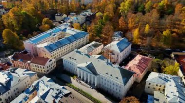 Aerial view of autumn trees in city and roofs of buildings. Colorful autumn trees during sunset, View of Tartu University, Estonia. Forest leaves changing color in Autumn. Tartu University hall. 