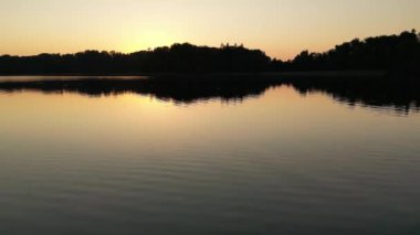 Flying low over an lake, water as the sun sets on the horizon. Small waves. Sunny sunset over the sea. Aerial view of drone flight over the water revealing the beautiful bog. Summer twilight hour.