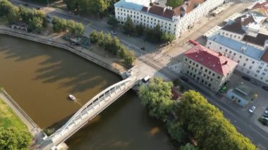 Şehir manzarası. Eski kasaba manzarası. İnsansız hava aracı insanların yaz günbatımında köprüden geçişlerini gösteriyor. İnsansız hava aracıyla uzaklaşıyorum. Yeşil şehir. Estonya, Tartu. Kırmızı çatıdaki binalar. Ortaçağ. 