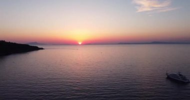 Colorful sunset above the sea surface with sail boat, sun goes down, blue and orange clouds flow in sky. Small yacht boat sailing in calm open sea at sunset. Floating on Sea Surface Golden Sky. 