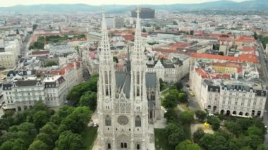 Viyana, Avusturya 'daki Votivkirche' in hava manzarası. Viyana 'daki Votiv Kilisesi, Votiv Kilisesi' nin güzel dış görünüşü. Parkta yeşil ağaçlar ve bulutlu gökyüzü. Avusturya, Viyana. Başkent. - Evet. Yüksek kalite 4k görüntü