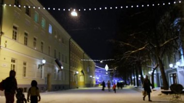 Sessiz ve rahat bir kasabada Noel arifesi, beyaz kar taneleri fırıl fırıl döner ve şehrin sokaklarına düşer. Sokakta yürüyen insanlar. Kar yağarken sakin bir kış gecesi. Noel tatili ışıkları. Tartu, Estonya.