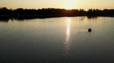 Hava aracı günbatımı gölündeki bir teknenin üzerinde alçaktan görünüyor. Gölde günbatımı kanosu. Sakin bir yaz akşamında vahşi doğada spor faaliyetleri. Arka planda güneş ışığı olan Teknede Aşk Hikayesi.