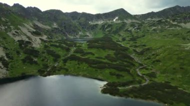 Sisli dağların üzerinde gün doğumunu ve Tatra 'daki Morskie Oko gölünü kucaklıyor. Bulutların üzerinde süzülüyor, görkemli dağ manzarasında yemyeşil manzaraya ve ikiz göllere tanık oluyor. Zakopane, Polonya. Yüksek Tatra Dağları