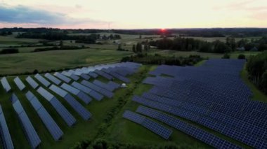 Güneş batımında güneş enerjisi çiftliğinde güneş enerjisini yeşil enerji için elektriğe dönüştüren fotovoltaik panellerle bir güneş enerjisi santralinin insansız hava aracı görüntüleri, Estonya 'da yaz günbatımı arka planında güneş panelleri.