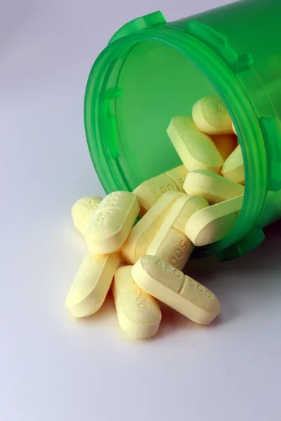 Green Prescription bottle of NSAID naproxen tablets spilling onto grey table