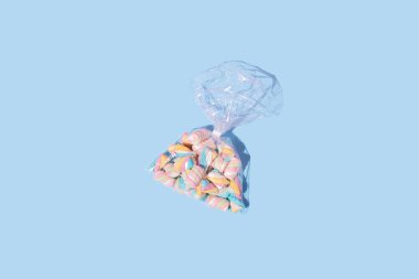 Pastel mavi arka planda şeffaf plastik torbaya sarılmış şekerlemeler. Tatlı yemek konsepti.
