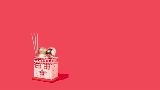 赤い背景に輝く光沢のある黄金のクリスマスボールとスパークラー付きのミニチュアホワイトハウス クリスマスやお正月のお祝いアイデア — ストック動画