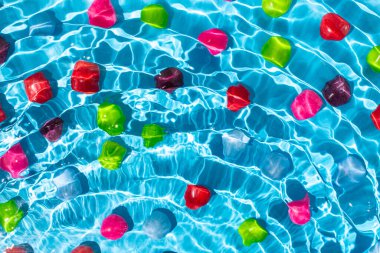 Dalgaların altında çok renkli şekerler, parlak mavi arka plan. Yaz rengi kavramı.