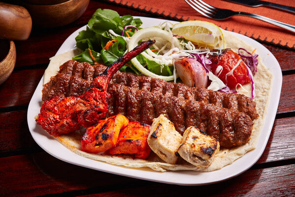Mixed Tandoori Grills platter with tikka boti kabab, salad, lemon and bread served in dish isolated on table side view of middle east food