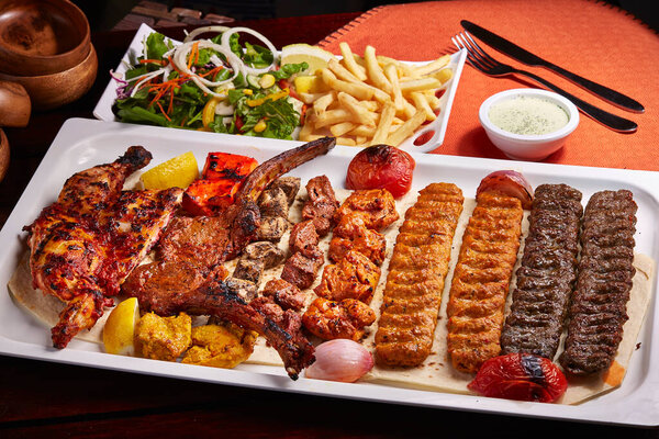 Spicy bbq Mixed Grills platter with tikka boti kababs, fries, salad and raita served in dish isolated on table side view of middle east food