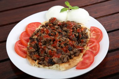 Ekmek ve domates dilimli İskander Kebap. Orta Doğu yemekleri masasının yanında izole edilmiş bir tabakta servis ediliyor.