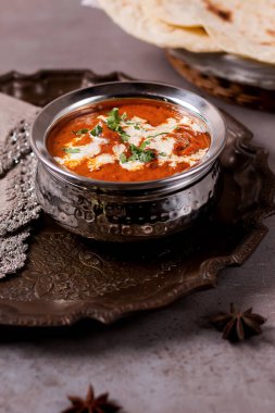 Masada servis edilen tereyağlı tavuk Makhani Masala, Arap yemeklerine bakıyor.